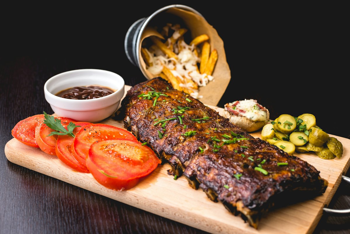 Geschmorte Spareribs auf Holzbrett mit Tomaten, Pommes und Beilagen