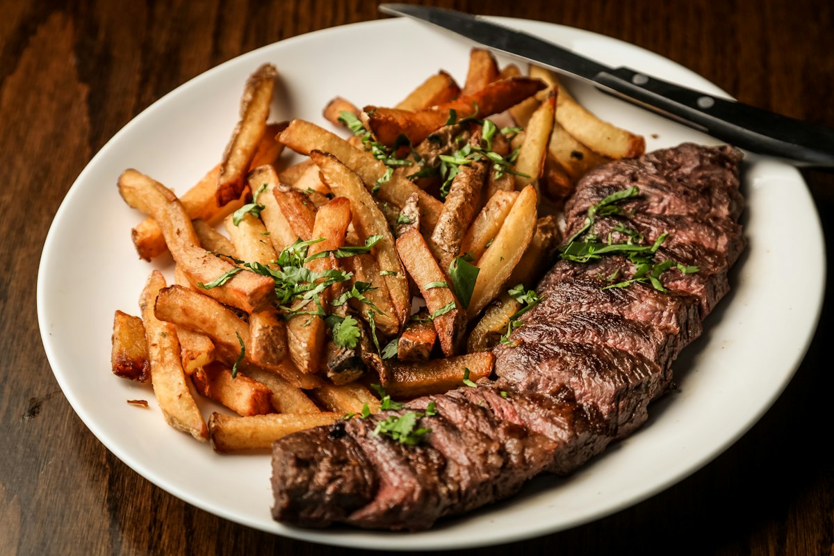 Saftiges Steak mit knusprigen Pommes und frischen Kräutern auf dem Teller