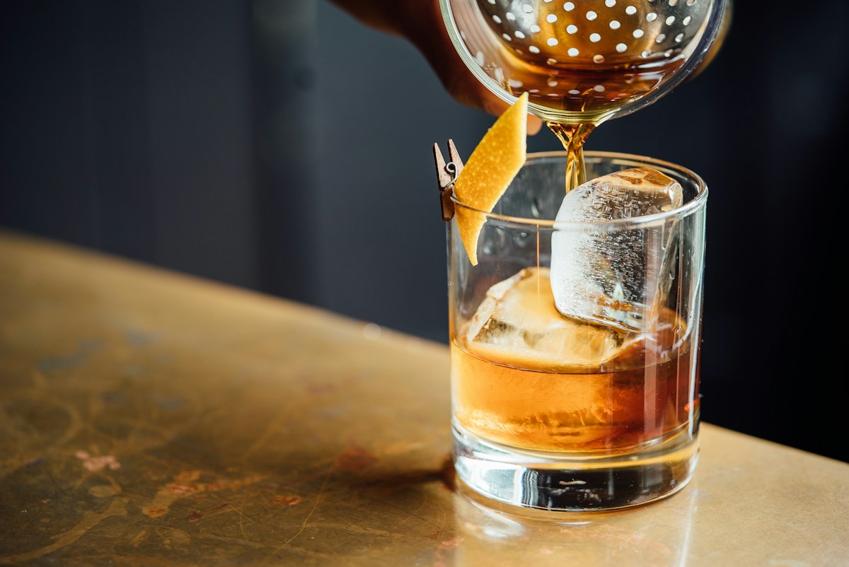 Frisch gemixter Cocktail mit Orangenzeste, der durch ein Barsieb ins Glas läuft